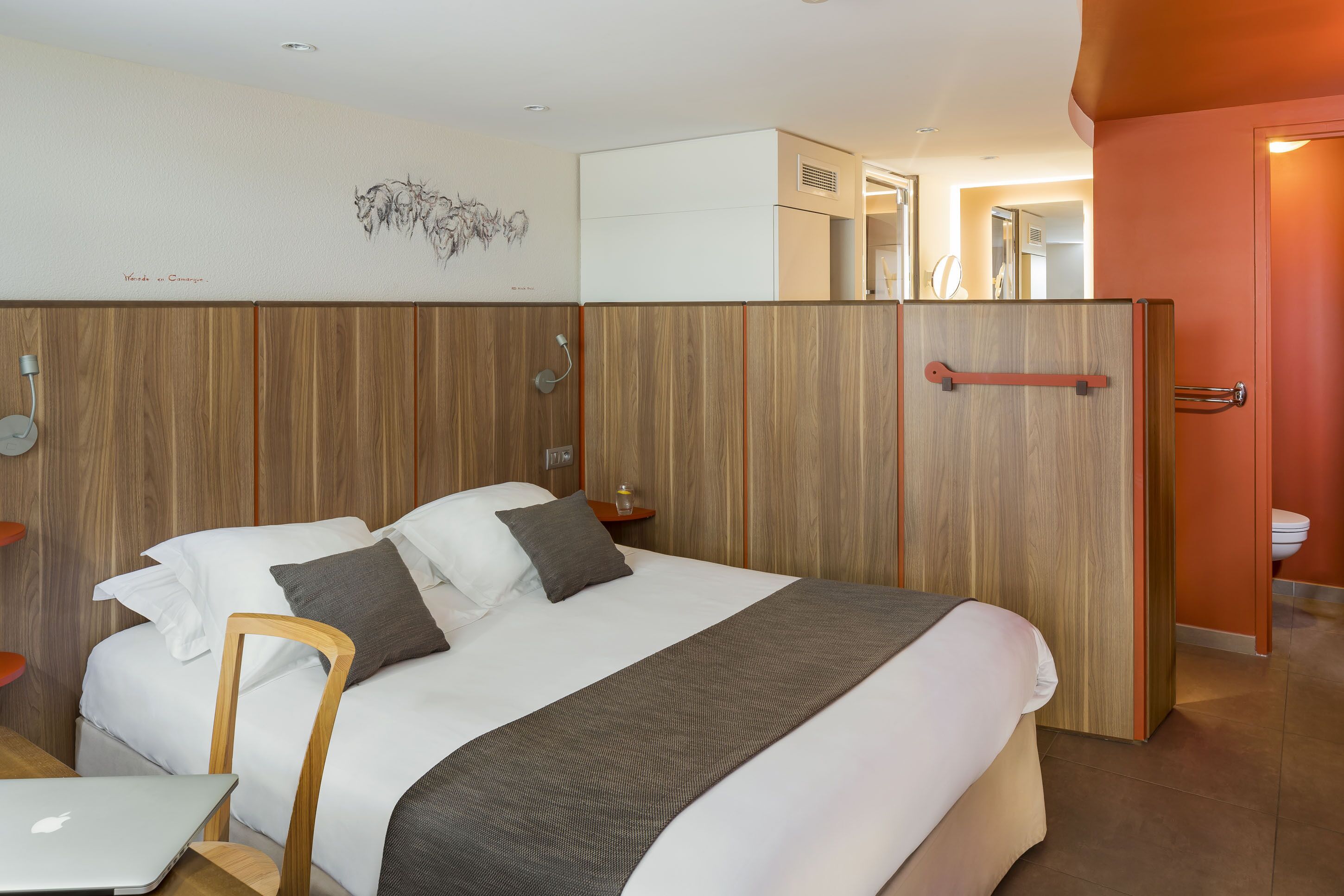 Une chambre d’hôtel moderne avec un grand lit, un bureau avec un ordinateur portable, une tête de lit en bois et une armoire.