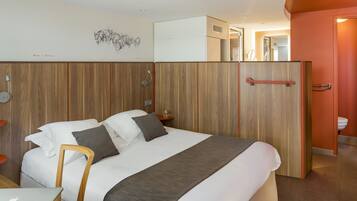 A modern hotel room with a large bed, a desk with a laptop, a wooden headboard, and a wardrobe.
