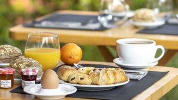 Una mesa de desayuno con croissants, un vaso de jugo de naranja, una taza de café y un plato con un huevo.