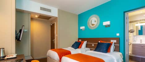 Habitación de hotel con dos camas, un escritorio y un baño visible a través de una puerta abierta.