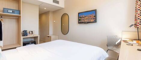 Habitación de hotel con una cama grande, un escritorio, una silla, un televisor y un armario.