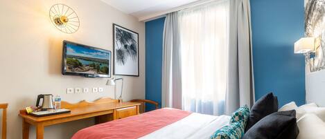 A hotel room with a bed, a desk, a chair, a coffee maker, a picture frame, and a window with curtains.