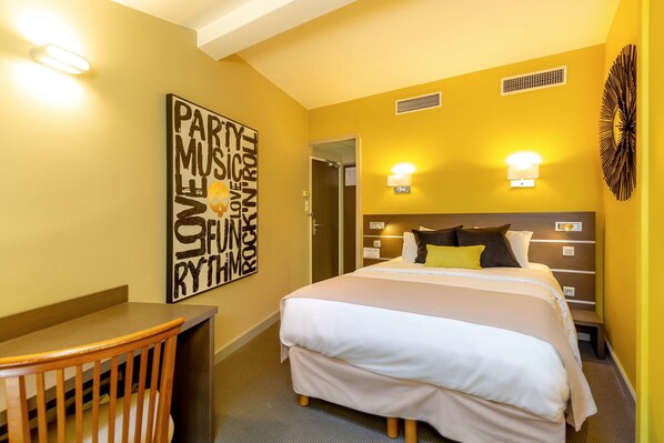 A hotel room with a bed, bedside tables, a desk, and a chair. There is a wall art piece and a decorative wall piece.