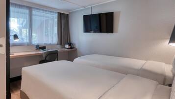 A hotel room with two beds, a desk, a chair, a TV, and a window with curtains.