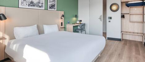 A hotel room with a large bed, a desk, a chair, and a wardrobe.
