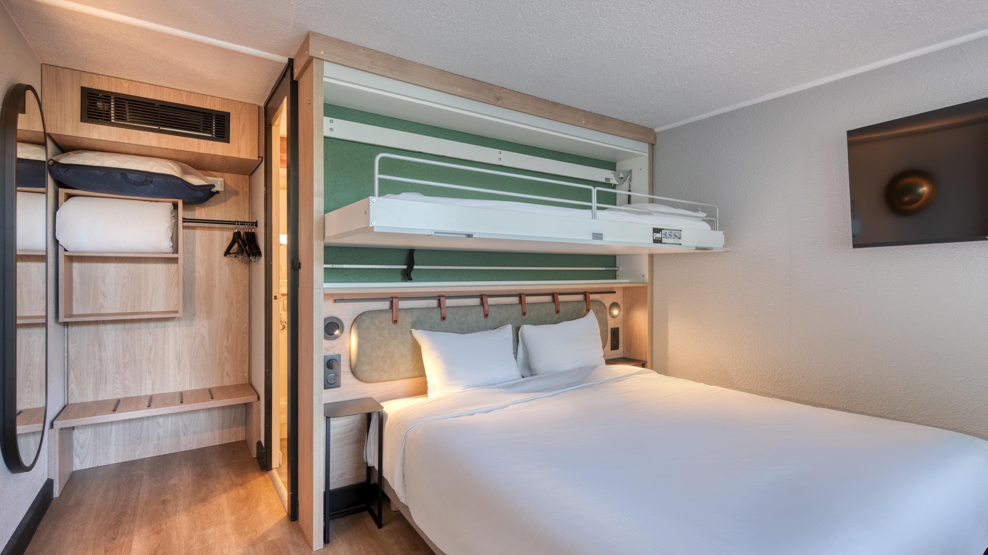 A bunk bed with a desk and shelving unit, a small table, and a wall-mounted TV.
