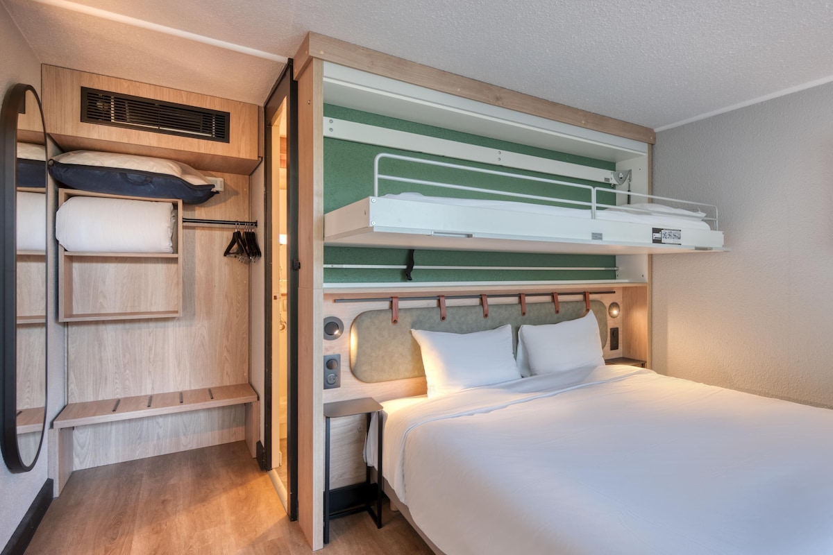 A bunk bed with a desk and shelving unit, a small table, and a wall-mounted TV.