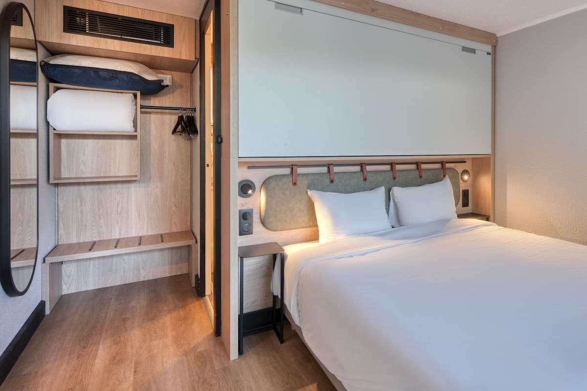 Une chambre d’hôtel comprenant un lit, une armoire, un miroir et un luminaire fixé au mur.