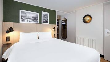 Una cama bien tendida con sábanas blancas, un cabecero con acabado de madera, dos lámparas fijadas a la pared y dos fotografías blanco y negro enmarcadas sobre la cama.