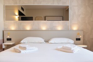 A hotel room with a large bed, two bedside tables, a mirror, and a wall-mounted light fixture. - Brit Hotel Avignon Sud (Avignon)