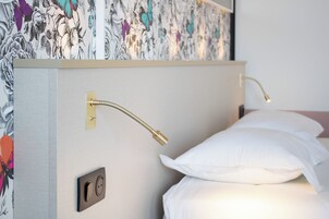 Una cama con almohadas blancas y cabecera con diseño de papel tapiz floral.