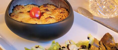 A bowl of food with a cherry on top, a salad with dressing, and a glass on a table.