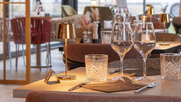 Un coin repas avec une table dressée pour quatre personnes, comprenant des verres à vin, des couverts et une lampe.