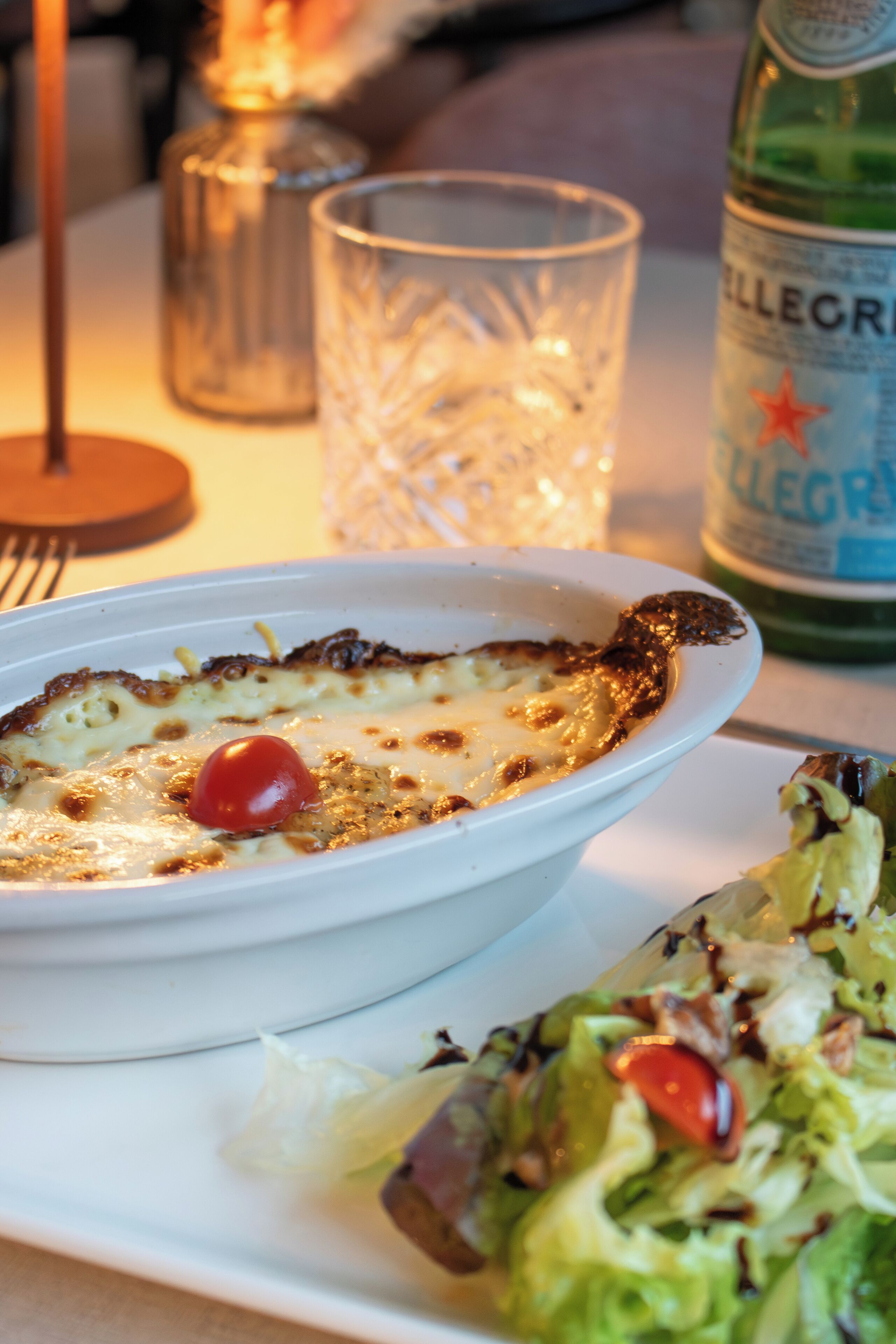 A white bowl of food with a cherry on top, a glass of water, and a bottle of water on a table.