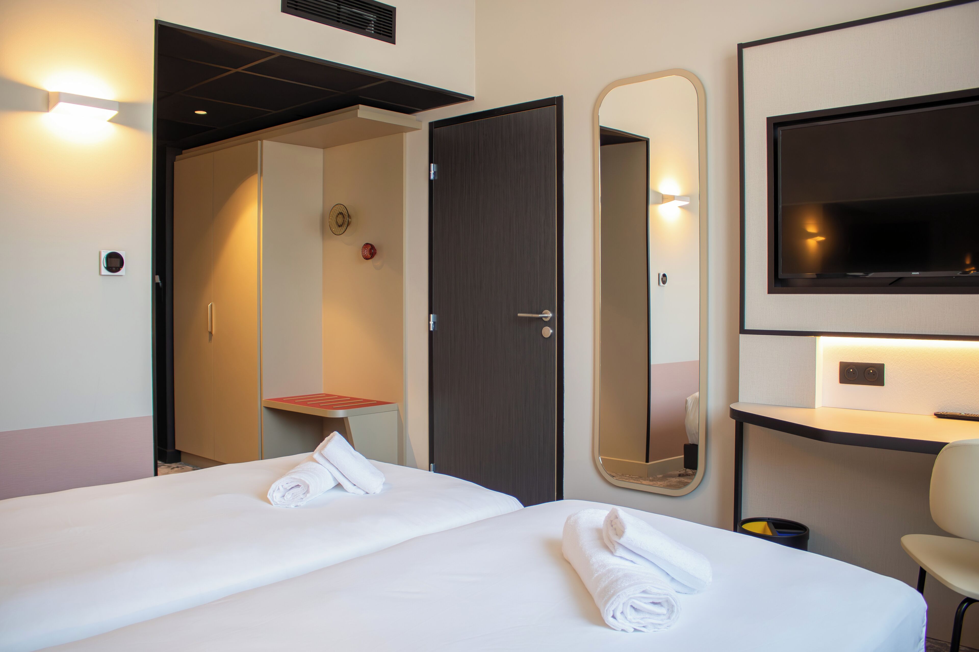A hotel room with two beds, a TV, a mirror, and a desk.