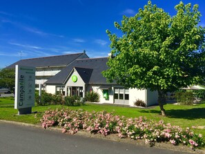 A hotel with a signboard, a large tree, and a flower bed. - Hotel Campanile Angers Ouest - Beaucouzé (Beaucouze)