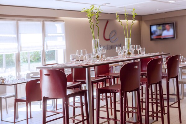 Un restaurante con una mesa larga dispuesta para comer, sillas rojas y altos jarrones con plantas verdes.