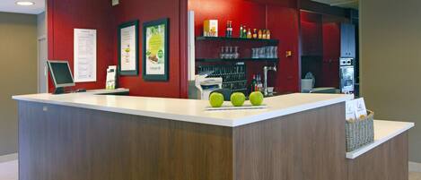 A reception desk with a wooden finish, a digital screen, and a counter displaying three green apples.