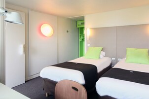 Habitación de hotel con dos camas, un escritorio, una lámpara y una pared verde.