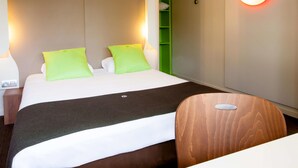 A hotel room with a bed, green pillows, a wooden chair, and a wall-mounted light. - Hotel Campanile Angers Ouest - Beaucouzé (Beaucouze)