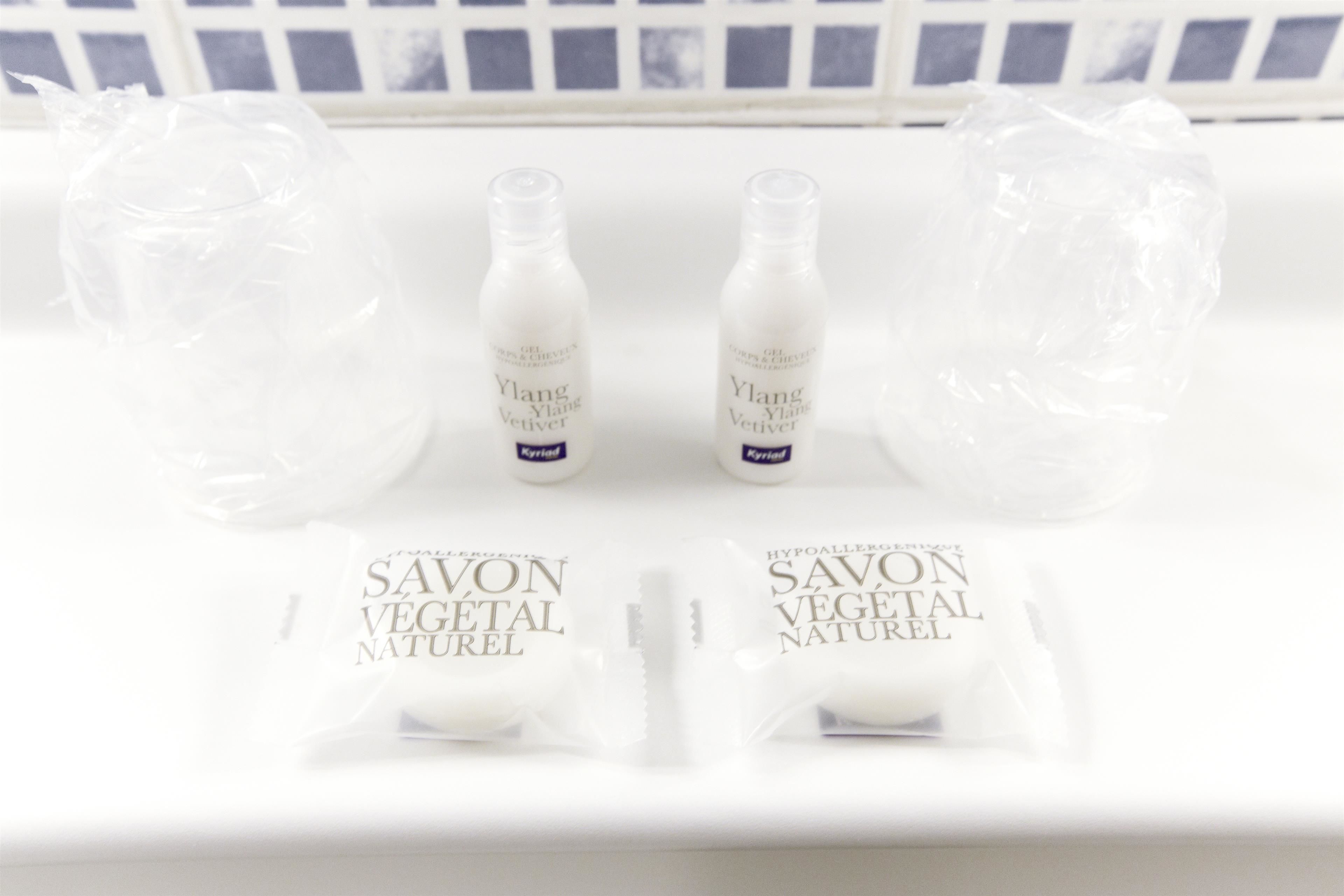 Een witte plank met twee flessen met de tekst 'Ylang Ylang Vetiver' en twee zakjes met de tekst 'Savon Vegetal Naturel'.