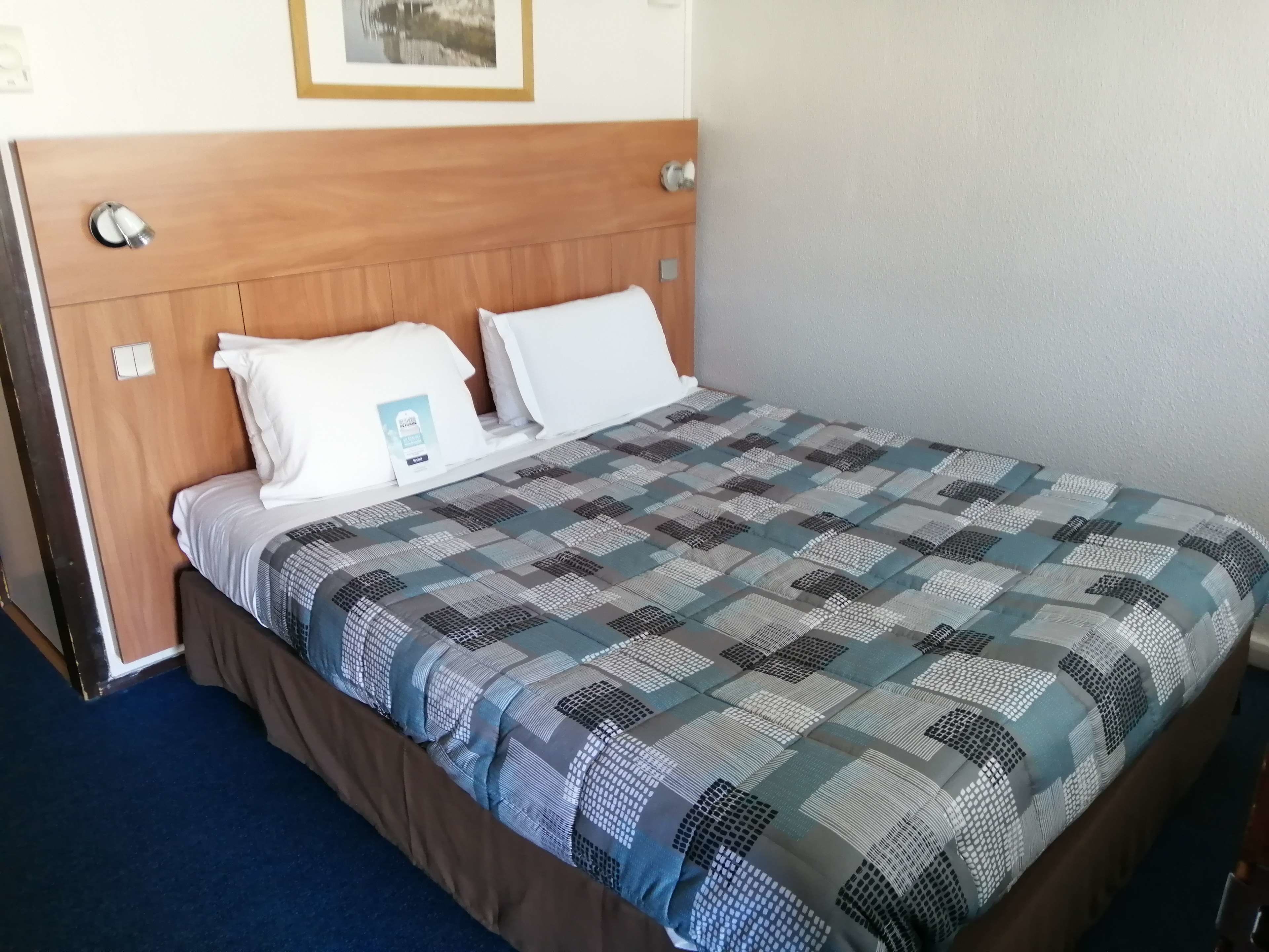 Una cama bien hecha con un edredón estampado, un cabecero de madera y almohadas blancas.