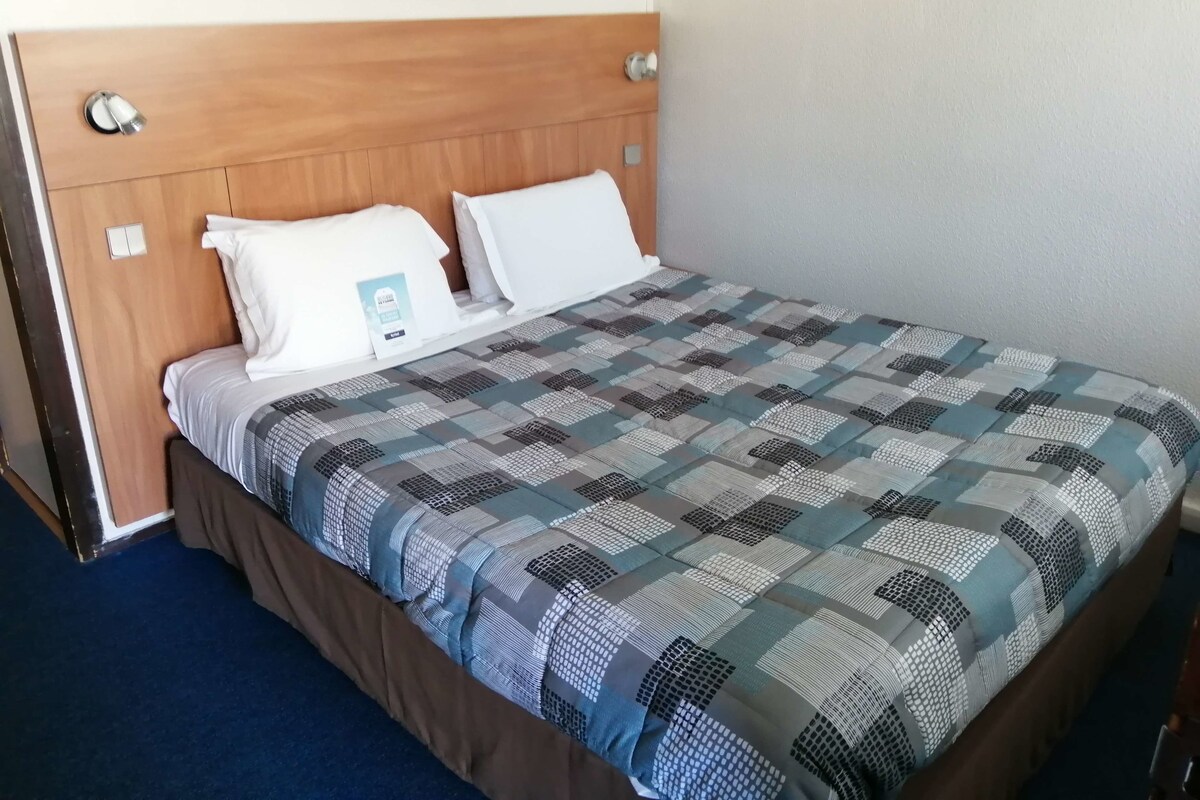 A neatly made bed with a patterned bedspread, a wooden headboard, and white pillows.
