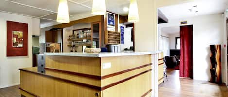 Un'area reception con un bancone in legno, illuminazione a sospensione e un cartello di uscita di sicurezza ben visibile.
