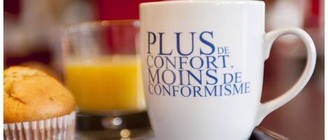 Eine weiße Tasse mit Schriftzug, ein Muffin und ein Glas Orangensaft auf einem Tablett.