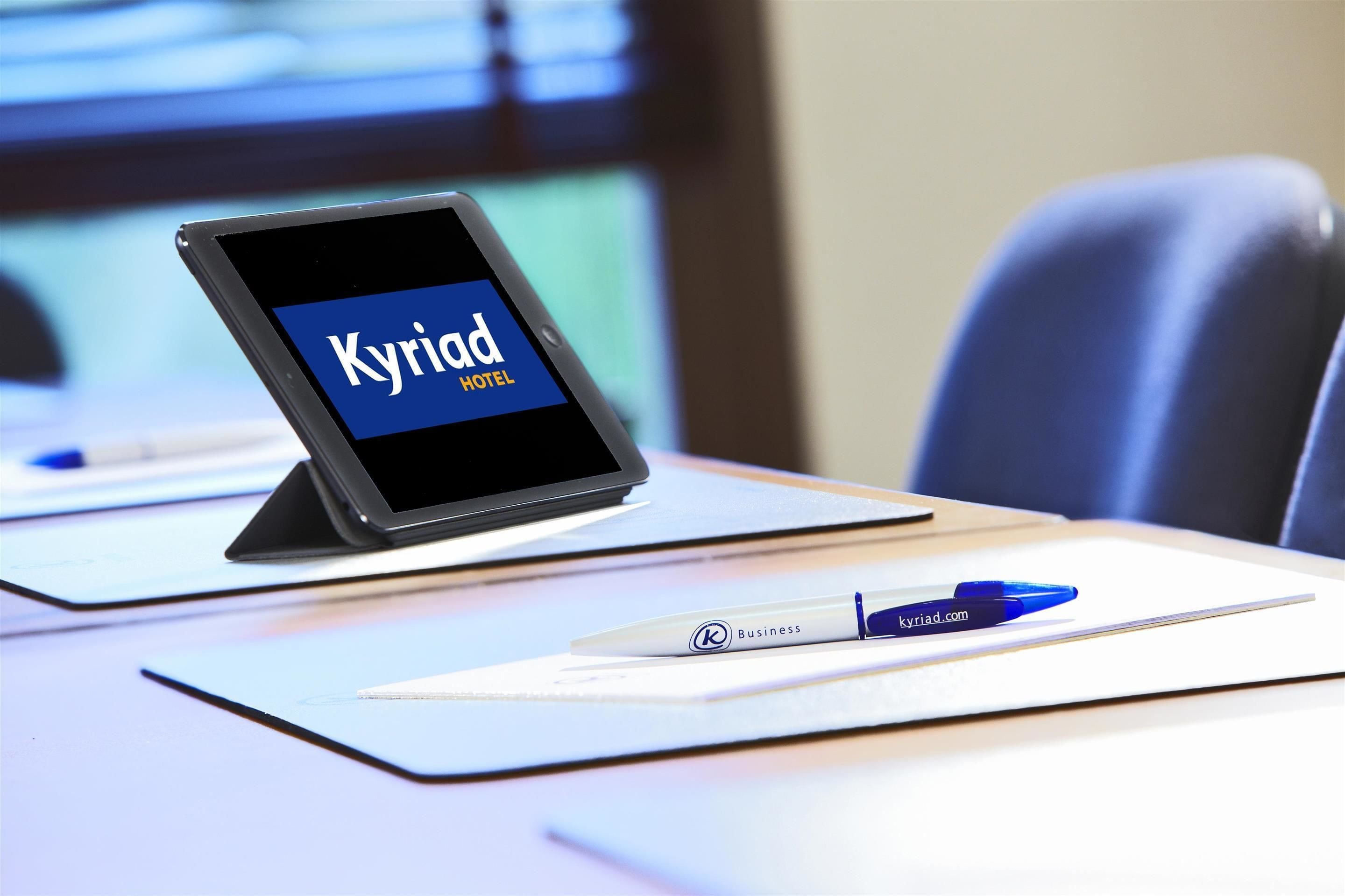 A tablet displaying 'Kyriad Hotel' on a desk with a pen and a notebook.