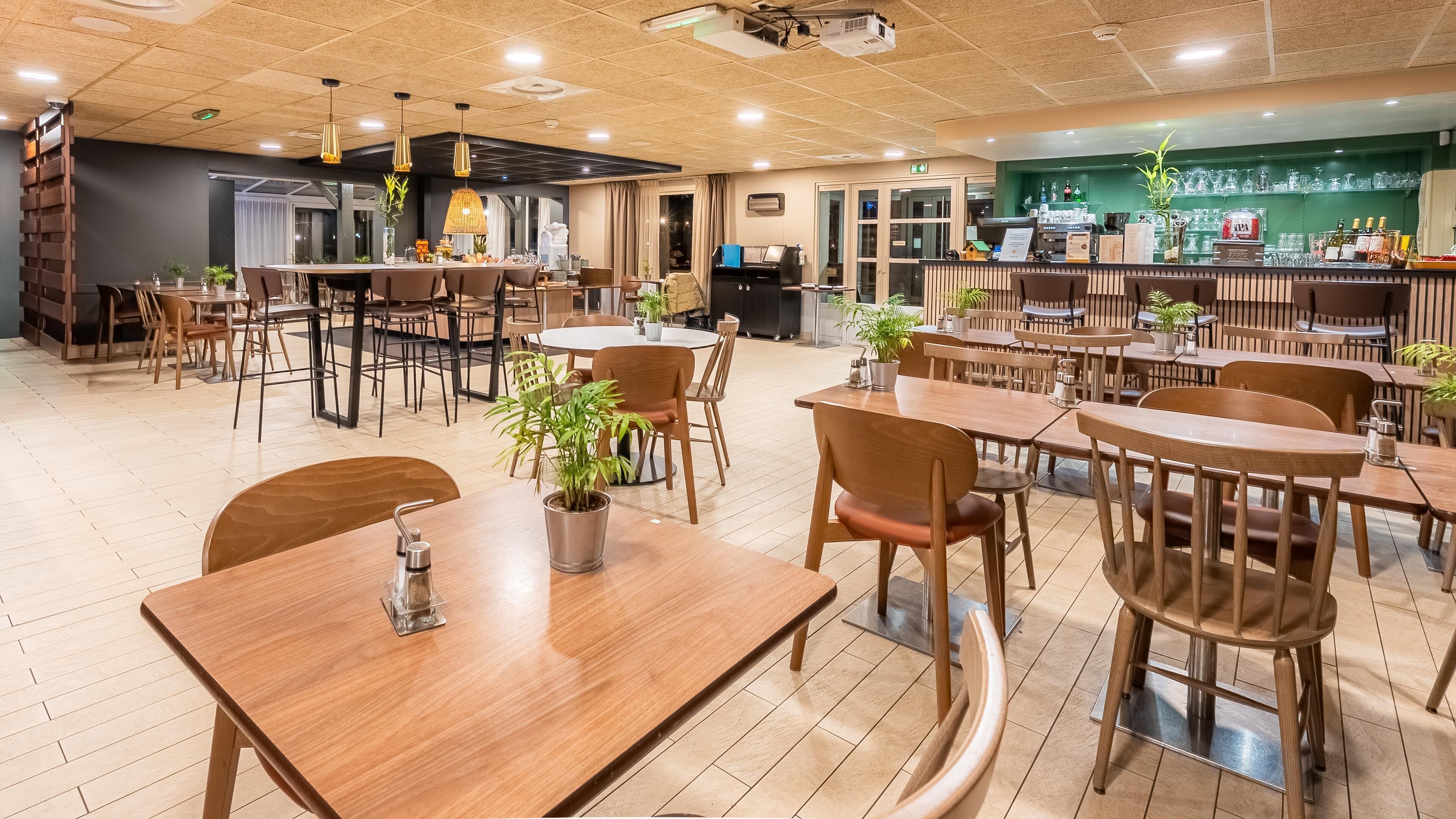 A restaurant with multiple dining tables and chairs, a bar area with a counter and bar stools, and potted plants.