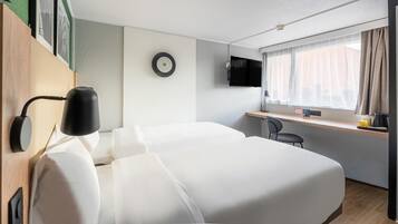 A hotel room with a bed, a desk with a chair, a television, and a window with curtains.