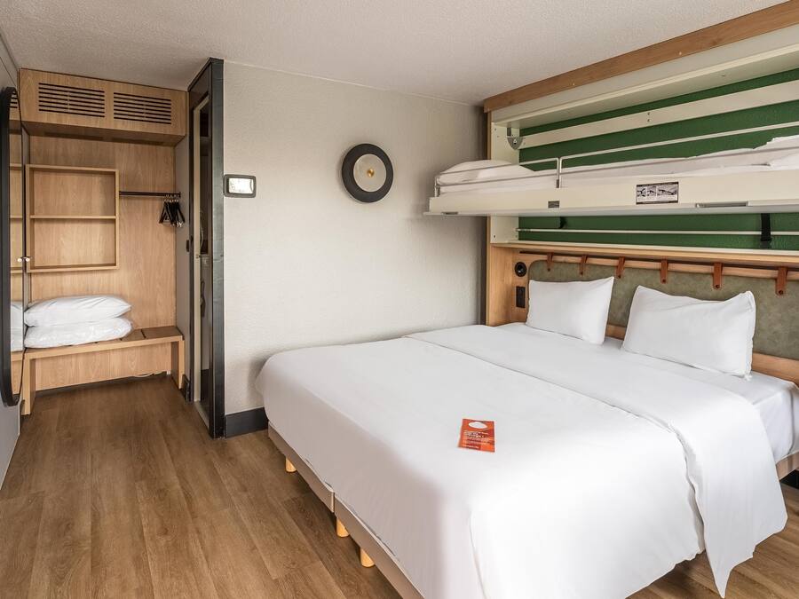 Una habitación pequeña con literas, un armario de madera, un banco y una mesita de noche.