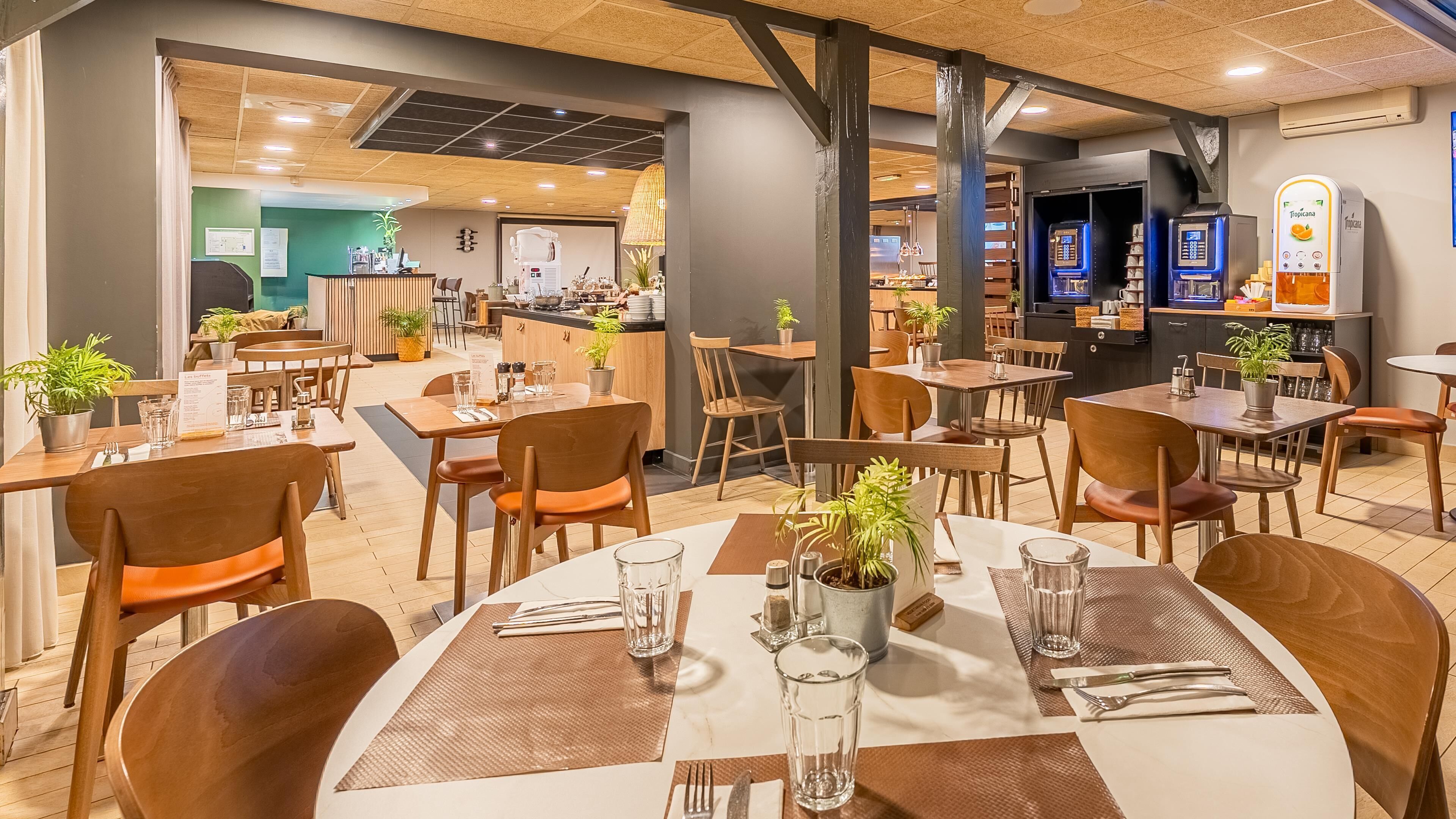 A restaurant with wooden tables and chairs, potted plants, and a counter area.