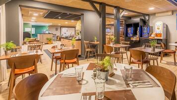 A restaurant with wooden tables and chairs, potted plants, and a counter area.