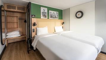 A hotel room with two beds, a wooden wardrobe, a green accent wall, and two framed pictures.