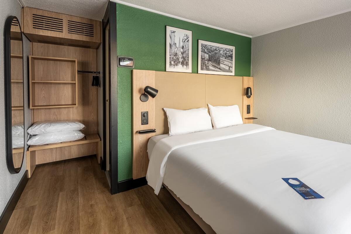 A hotel room with a large bed, wooden wardrobe, and a green accent wall.