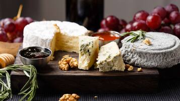 A variety of cheeses, grapes, walnuts, and a bottle on a wooden board.