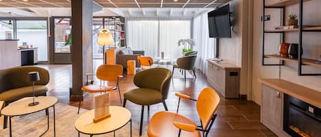 A modern hotel lobby with a seating area, a reception desk, and a television mounted on the wall.