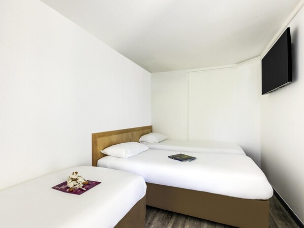 Une petite chambre d’hôtel moderne, dotée d’un lit simple, d’une table de chevet, d’un téléviseur à écran plat fixé au mur et d’une tête de lit en bois.