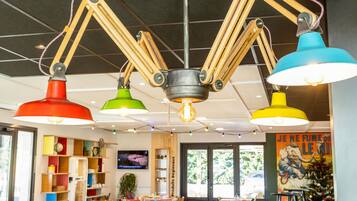 A restaurant interior with multiple tables and chairs, a television screen, and a variety of hanging pendant lights.