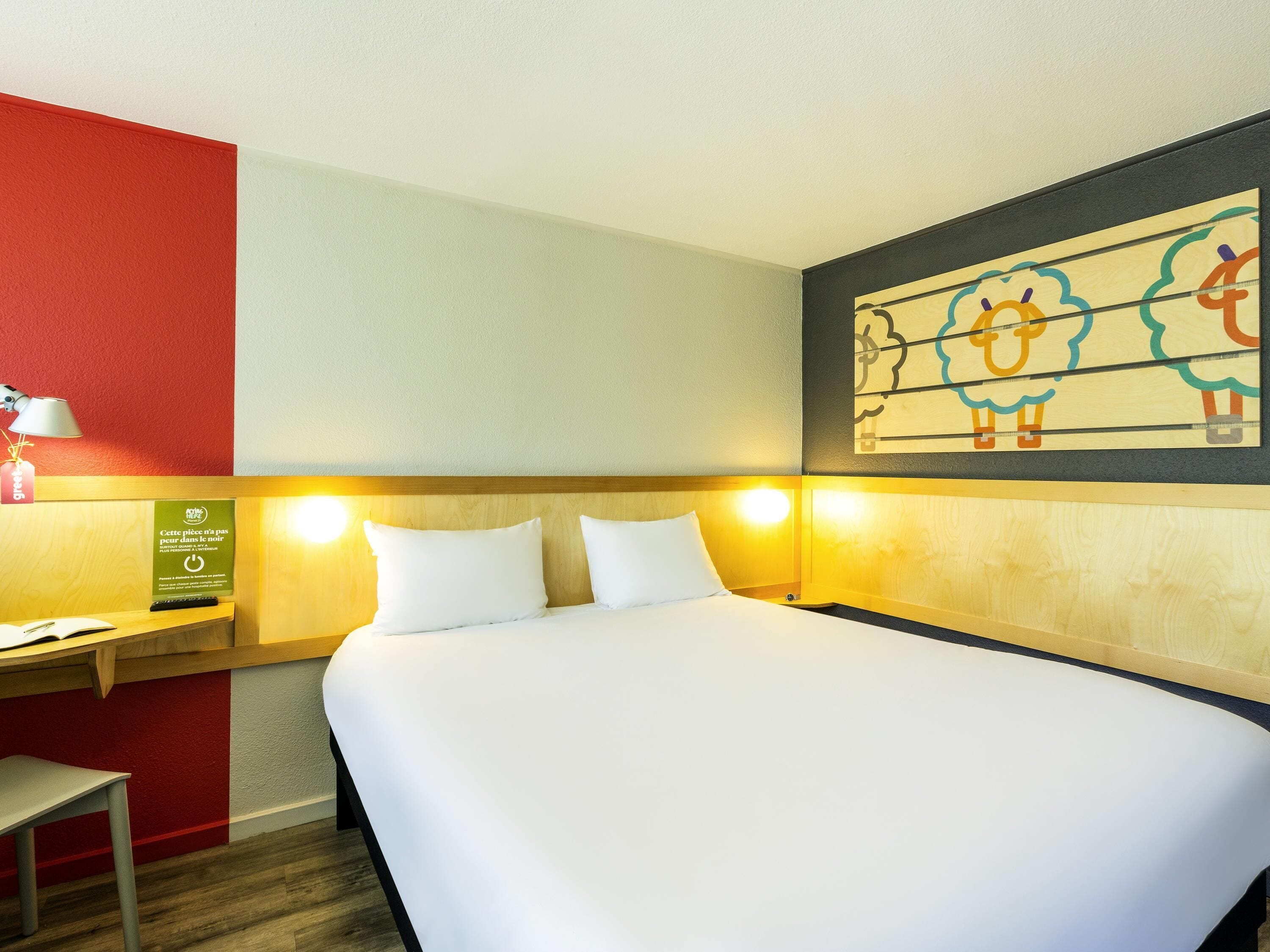 Habitación de hotel con cama, mesita de noche, lámpara y una obra de arte colgada en la pared.