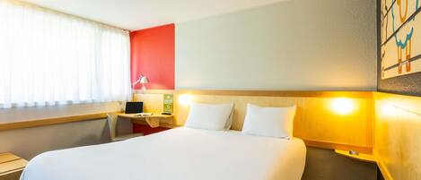 A hotel room with a large bed, a desk with a lamp, and a nightstand.