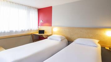 Habitación de hotel con dos camas, un escritorio, una silla, una lámpara y una ventana con cortinas.