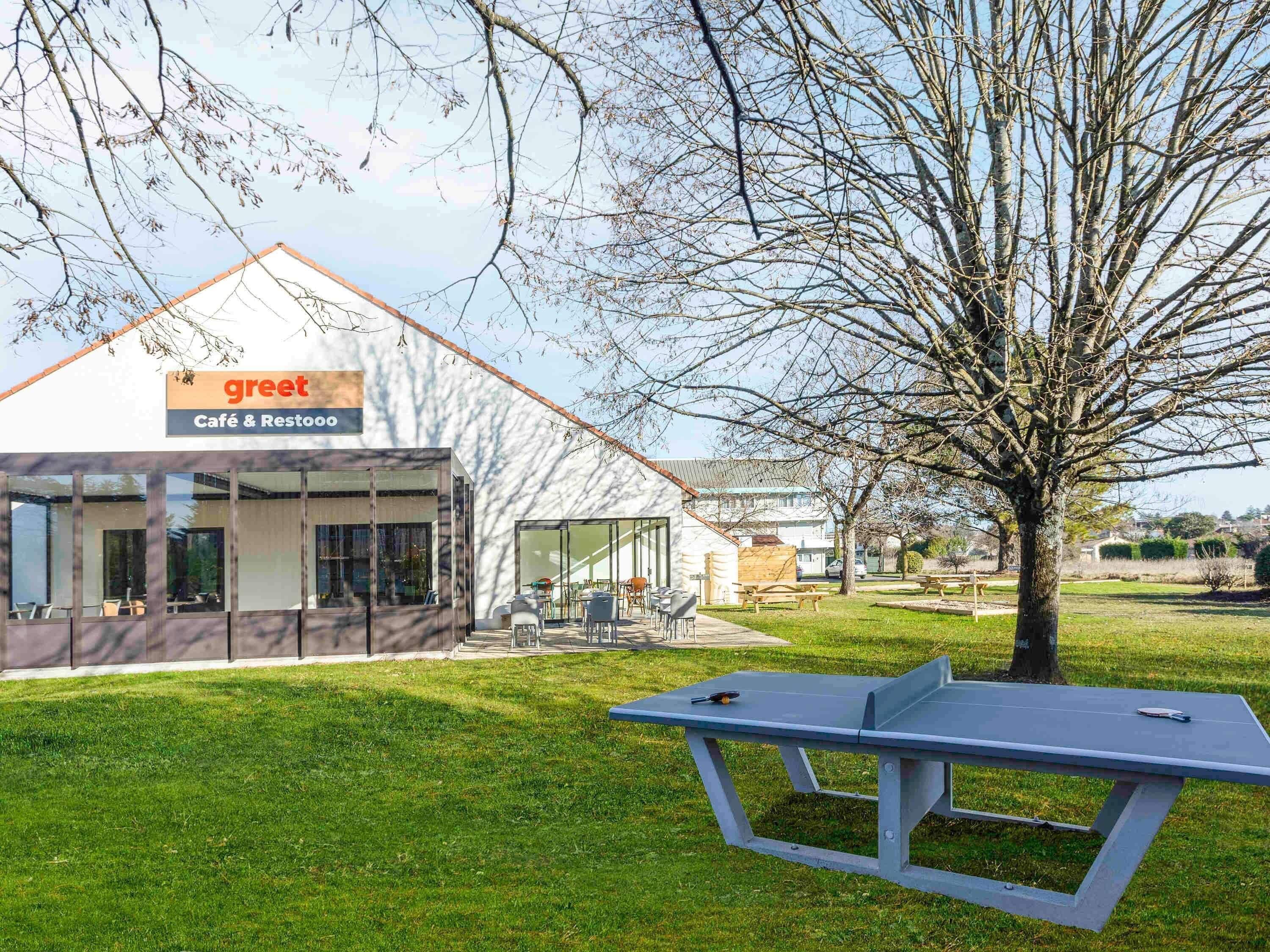 A modern building with a café and restaurant sign, outdoor seating, and a ping pong table.