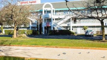 Un hotel con un cartel que dice 'greet hotel', un estacionamiento y una cancha de bochas.