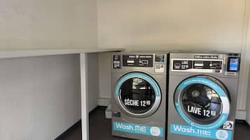 Two Wash.me Group washing machines with 12 kg capacity, located in a corner with a white wall and tiled floor.
