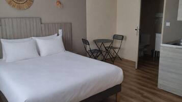 Une chambre avec un lit, un miroir rond, une petite table avec des chaises et un coin cuisine.