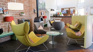 A modern lounge area with yellow and gray chairs, a small round table, and a brick-patterned wall with a mounted television.