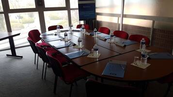 A conference room with a large table, red chairs, water bottles, and a sign for 'Kyriad Hotel'.